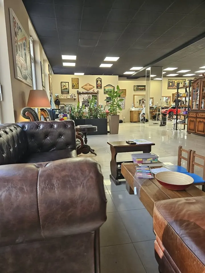 Interiér barbershopu: čierne kožené chesterfieldy, drevené stolíky, lampy a obrazy na stenách
